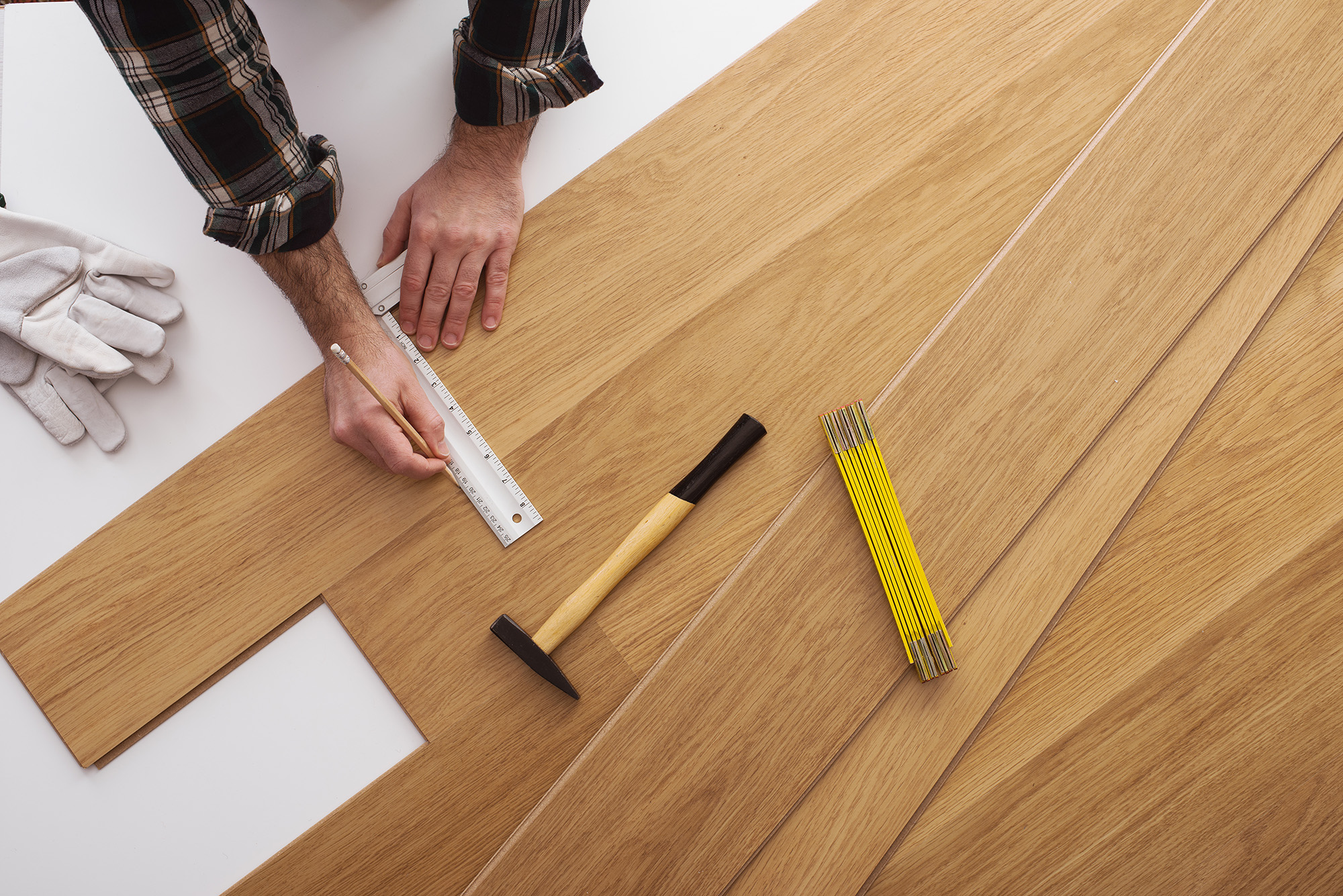 Carpenter installing a wooden flooring and measuring with a precision ruler, top view